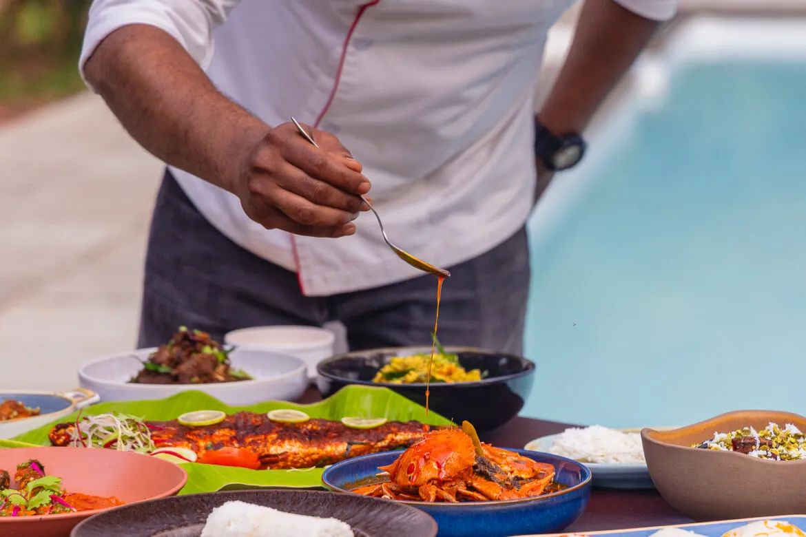 Chef plating a full South Indian seafood and meat spread poolside at Karma Vythiri