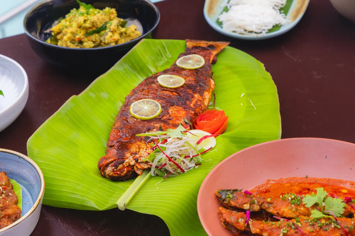 Whole grilled fish on banana leaf with lime garnish at Karma Vythiri restaurant