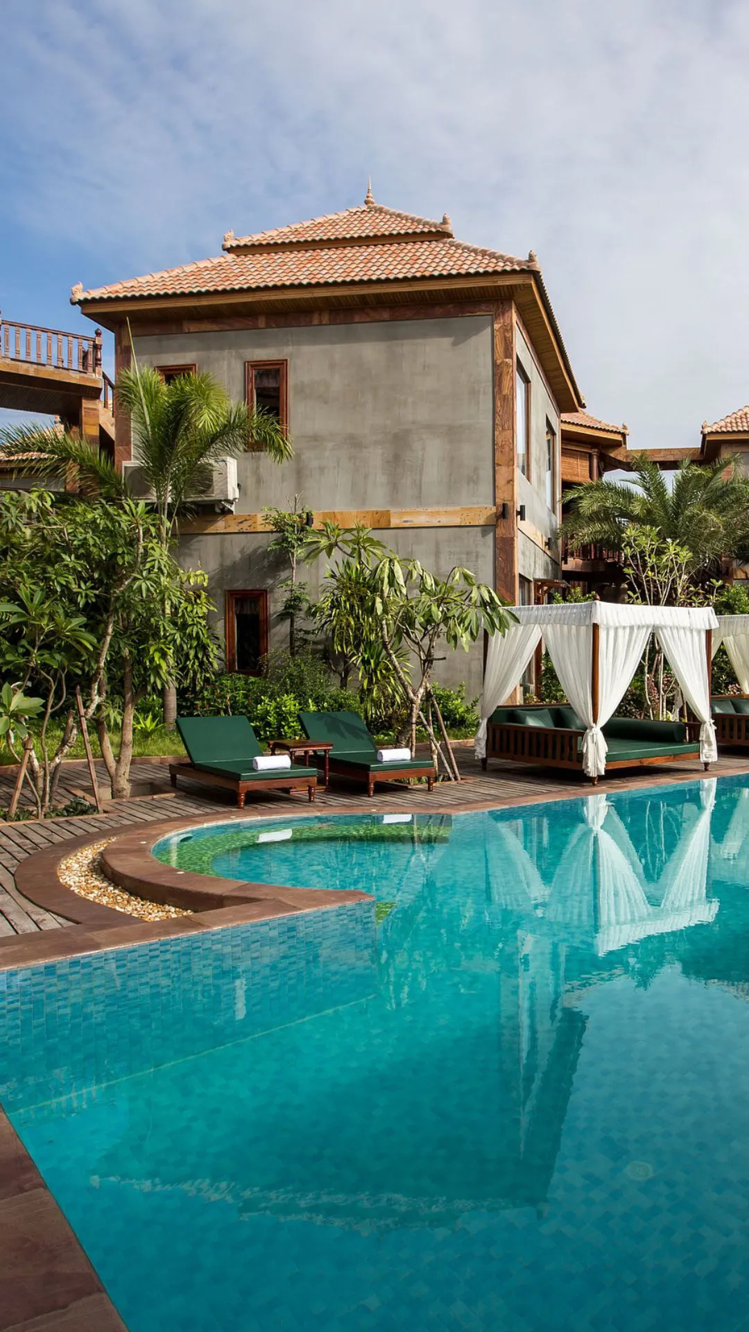 Poolside daybed cabana with curtains and resort building at Karma Bayon